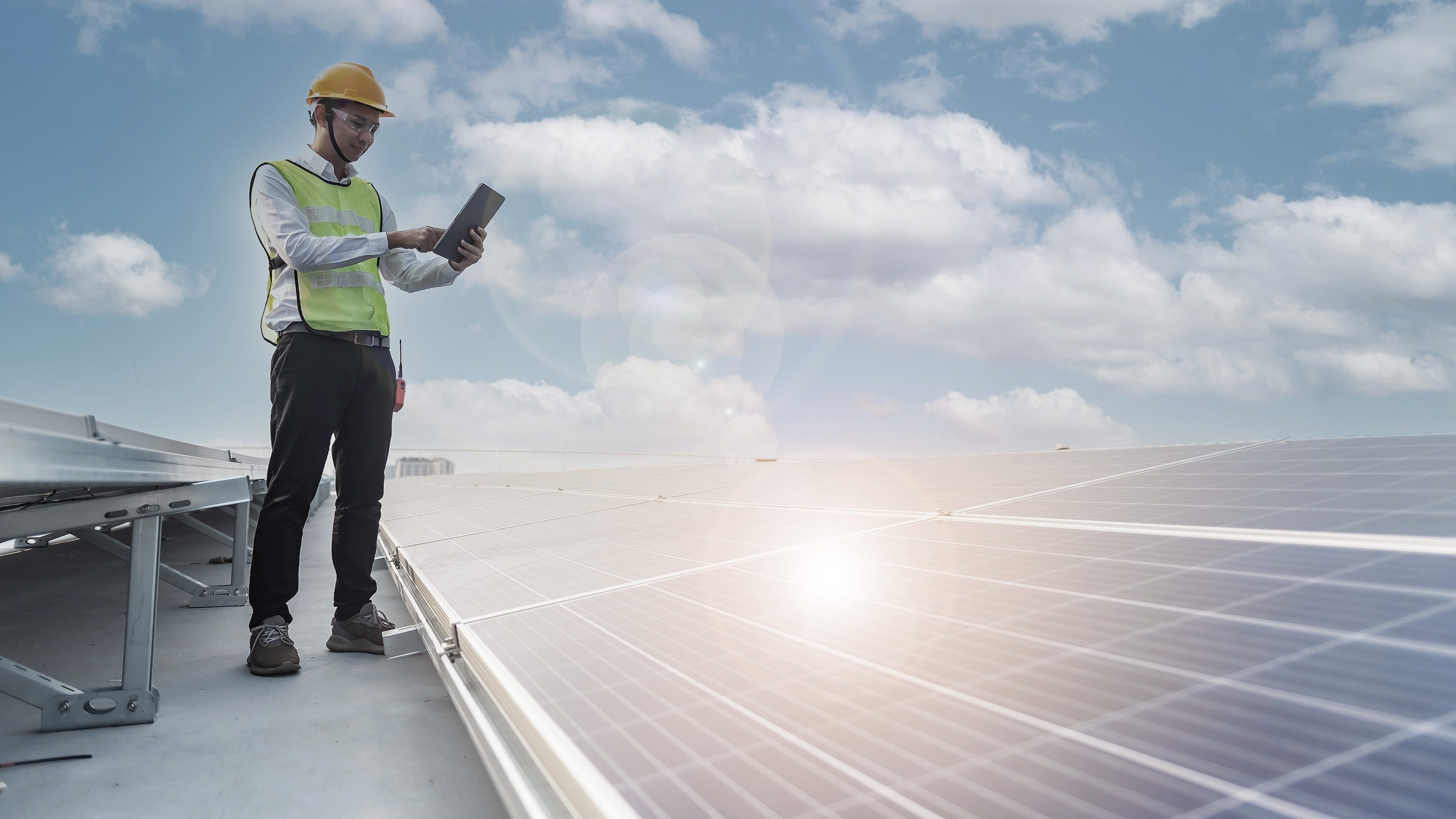 Ein Mann mit Helm und Warnweste auf dem Dach eines Hauses, der die Solarzellen überprüft.