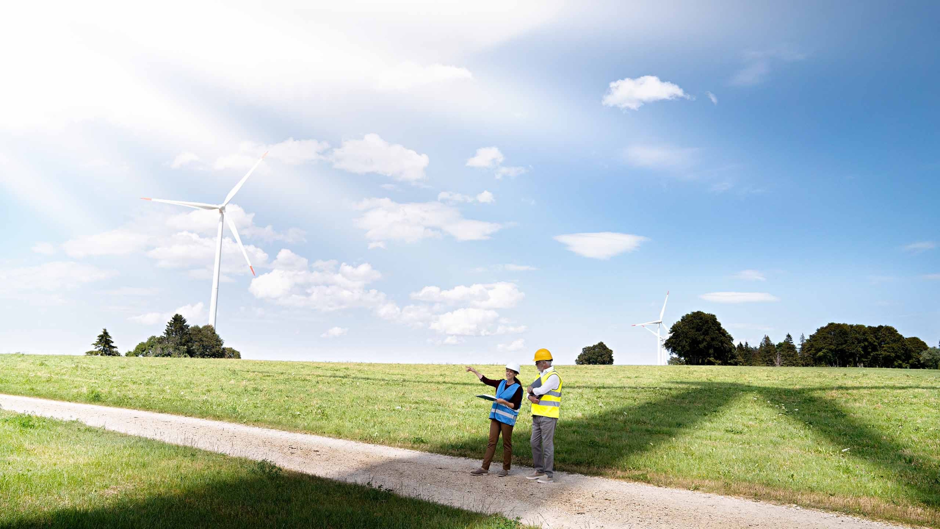 Ein Feld, auf dem zwei Personen, die Warnwesten und Helme tragen, die neuen Windräder planen.