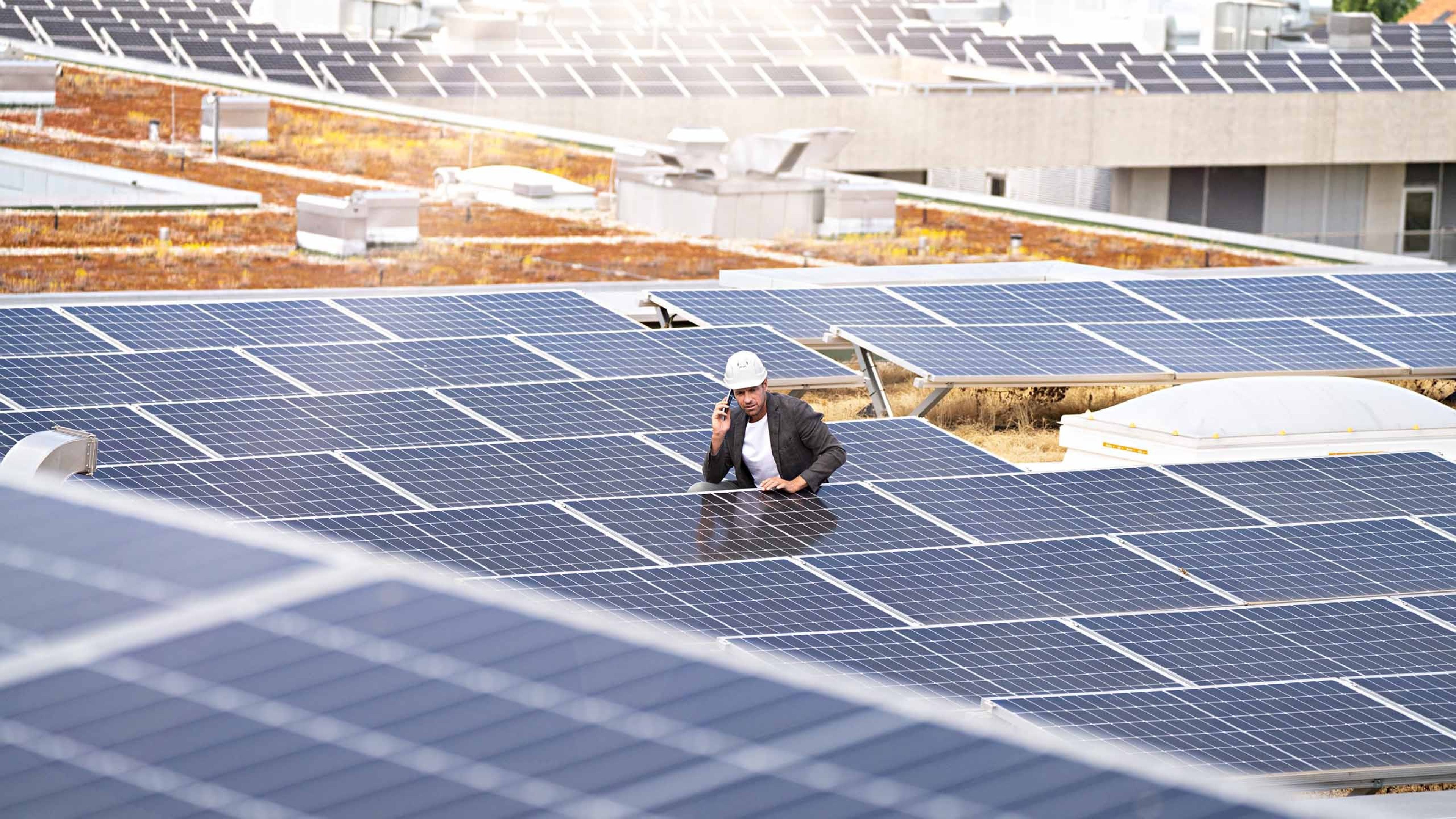 A man standing on the roof of a house equipped with solar panels.