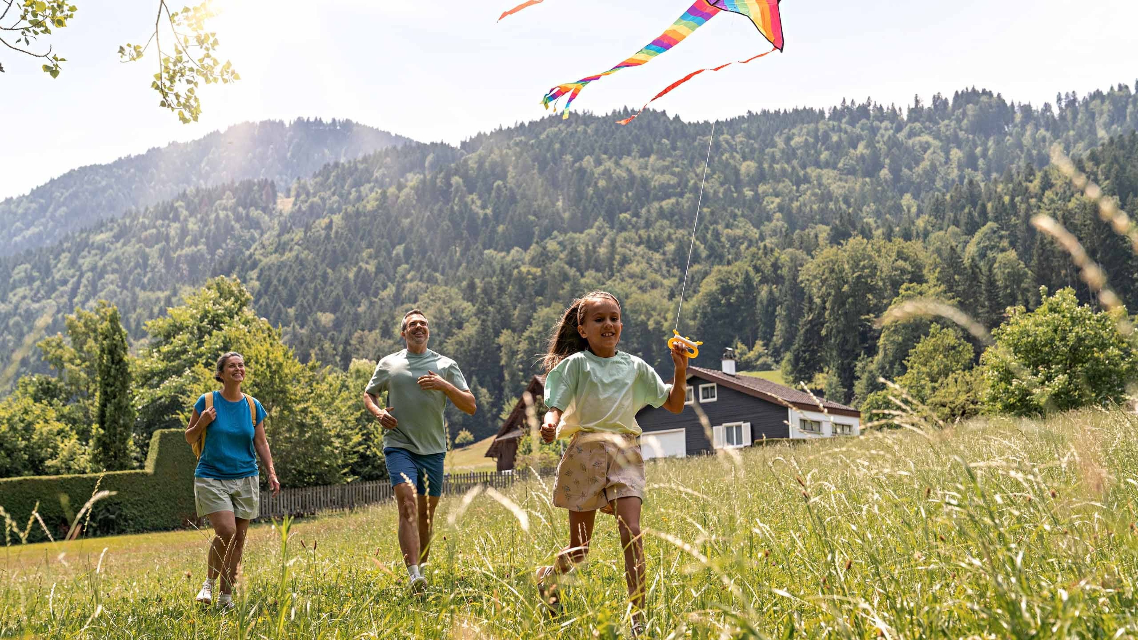 A family walking across a field while the daughter holds a kite in her hand.